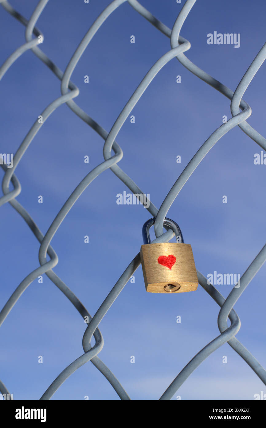 Locked padlock with heart hanging on a chain linked fence with a blue ...