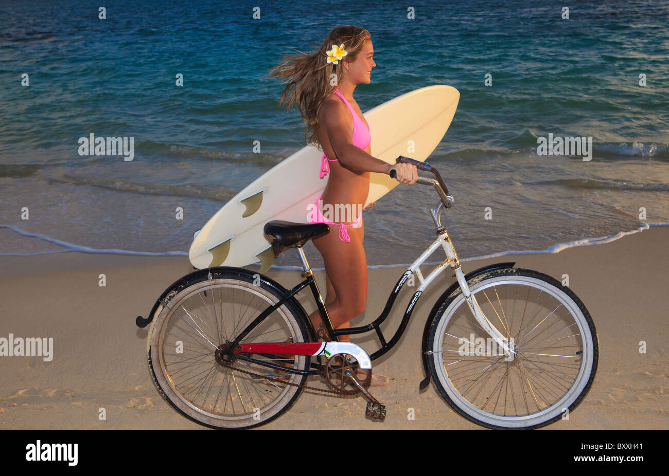 Blond Girl In Pink Bikini Riding Her Bike On The Beach In Hawaii With Her Surfboard Stock Photo