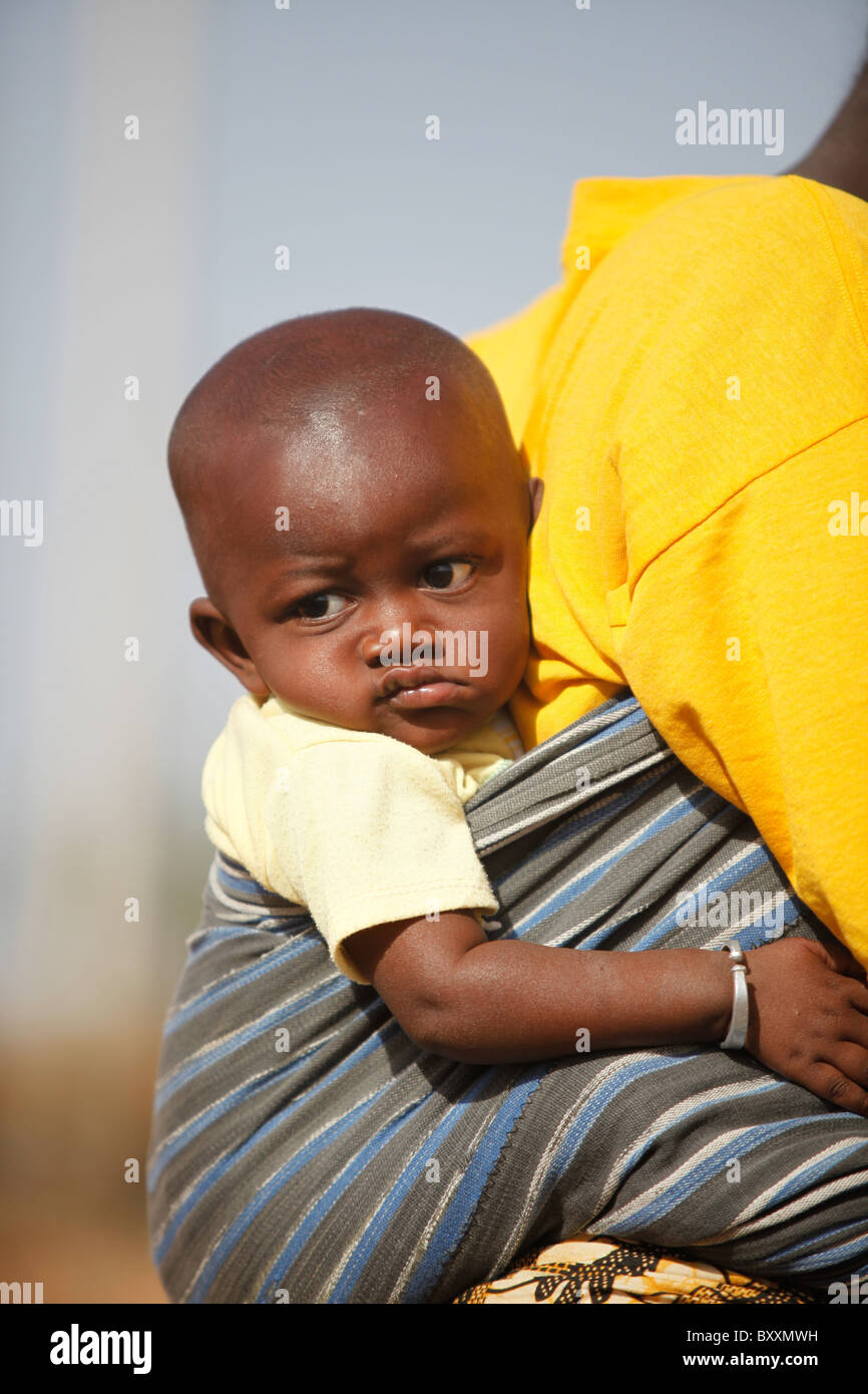 In the town of Djibo in northern Burkina Faso, a woman carries her young child strapped to her back. Stock Photo