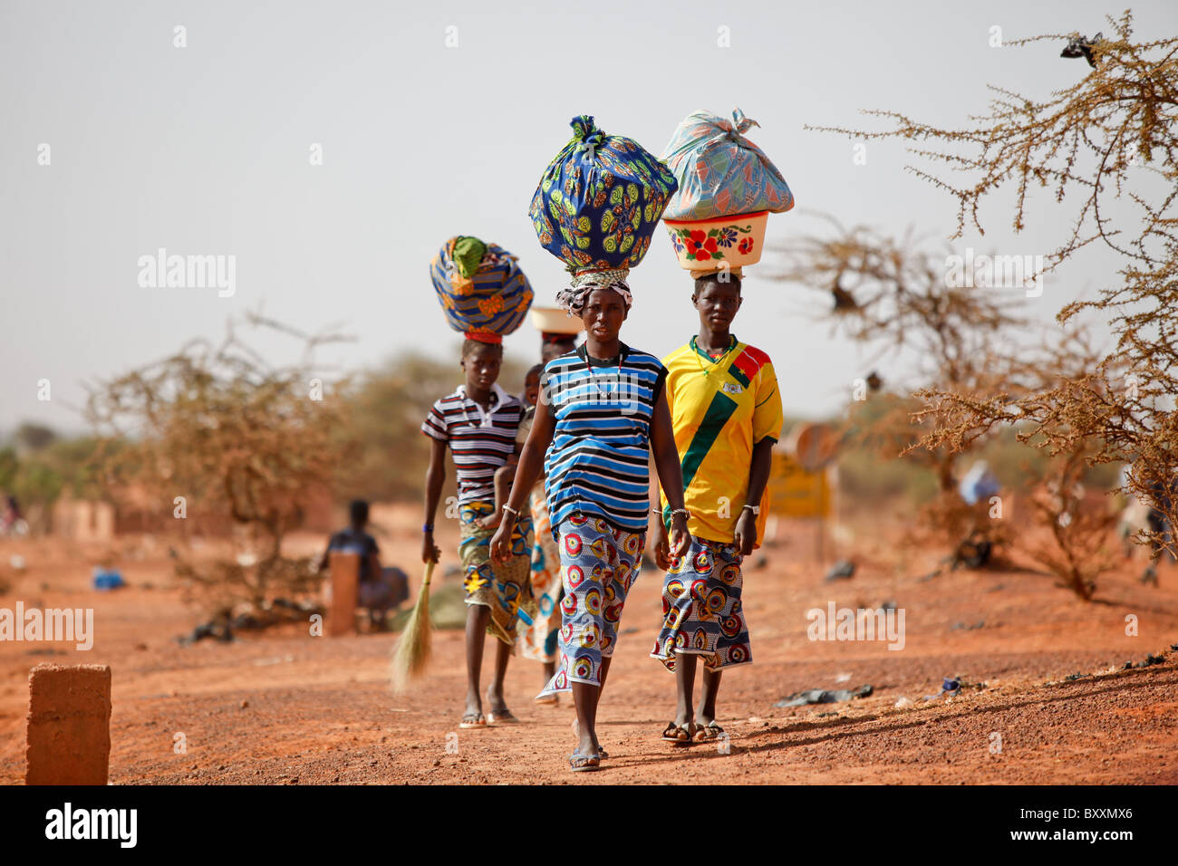 Women arrive in the town of Djibo, Burkina Faso on foot, carrying their wares on their heads in traditional African fashion. Stock Photo