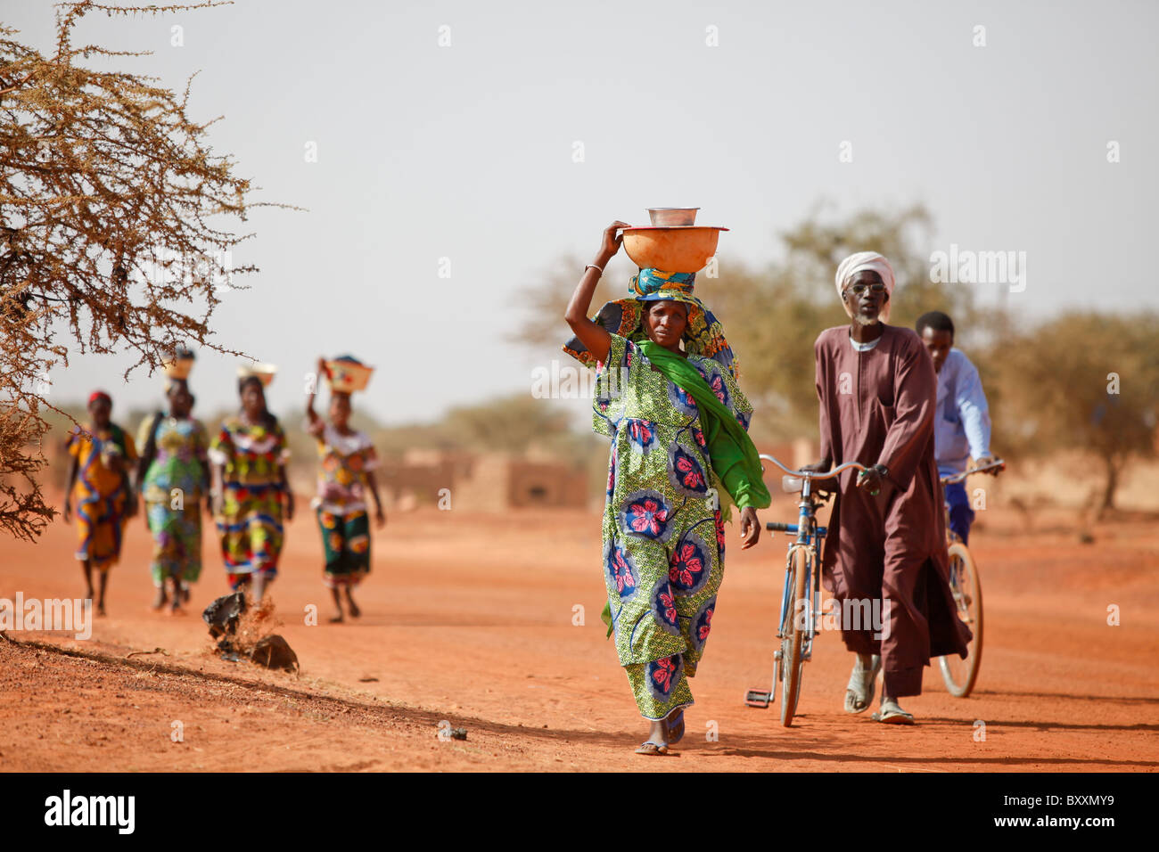 Women arrive in the town of Djibo, Burkina Faso, on foot, carrying their wares on their heads in traditional African fashion. Stock Photo