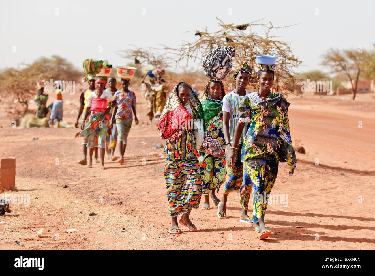 Women arrive in the town of Djibo, Burkina Faso, on foot, carrying their wares on their heads in traditional African fashion. Stock Photo