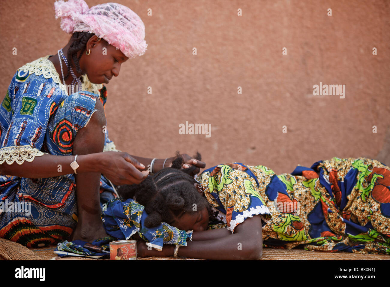 In the town of Djibo in northern Burkina Faso, a young woman braids her cousin's hair in traditional Fulani style. Stock Photo