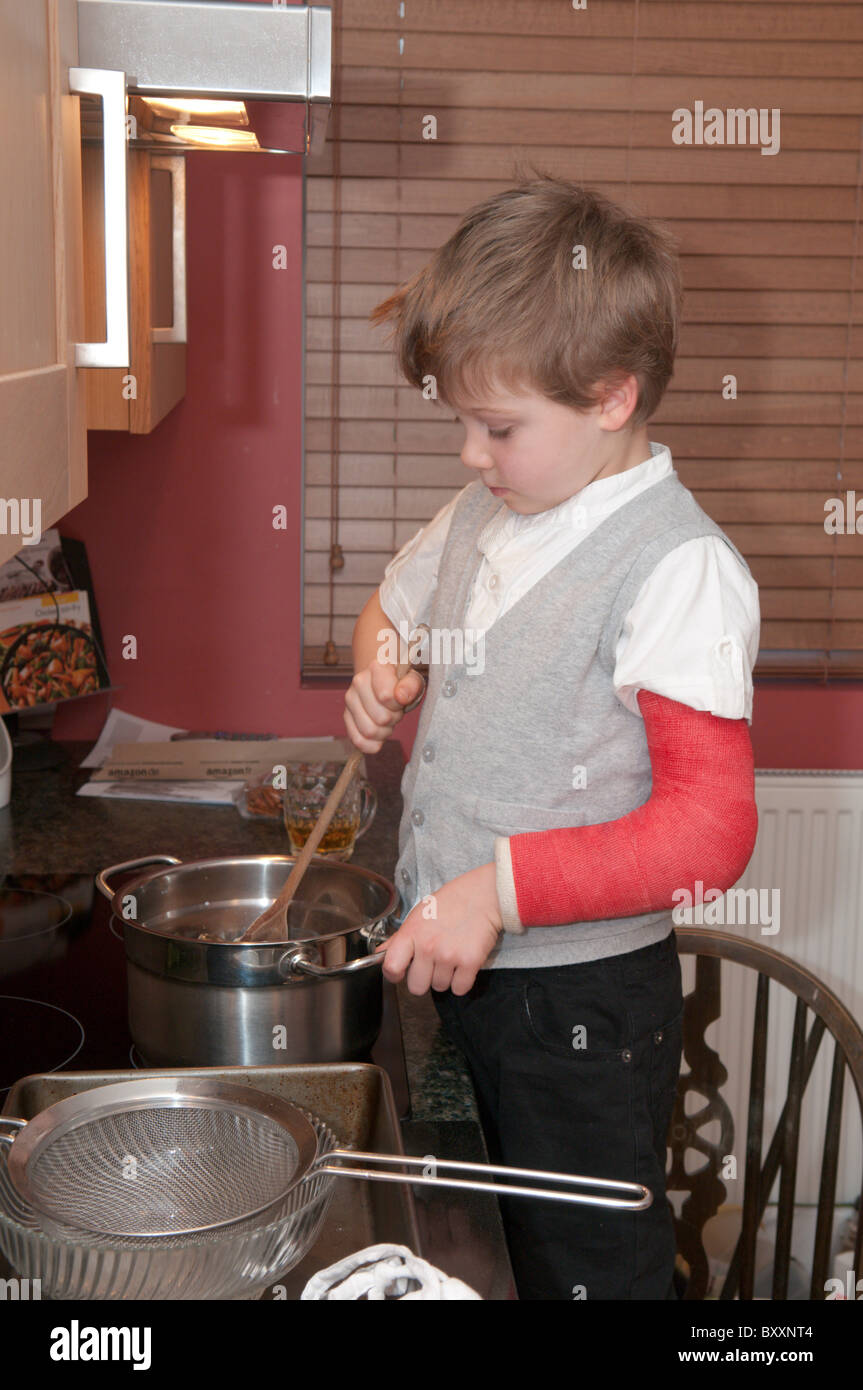 fouryearold boy with a broken arm cooking making cakes standing on a chair next to the