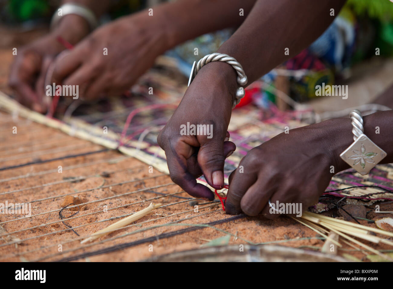 In the town of Djibo in northern Burkina Faso, two Fulani women weave a straw mat. Stock Photo