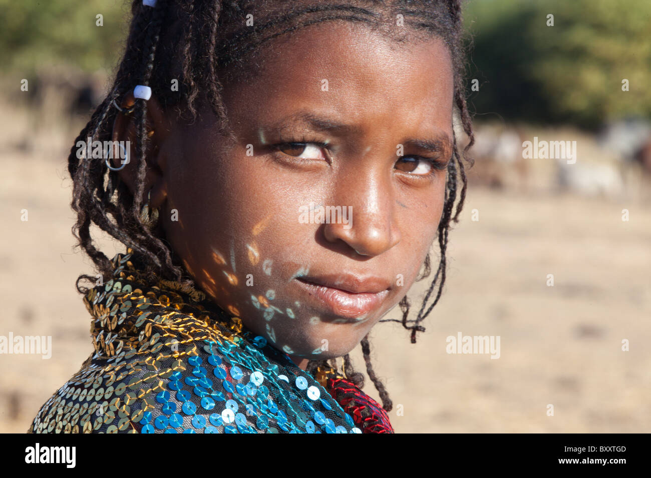In a seasonal Fulani village in northern Burkina Faso, reflections from the sequins of a young woman's shawl dance on her face. Stock Photo