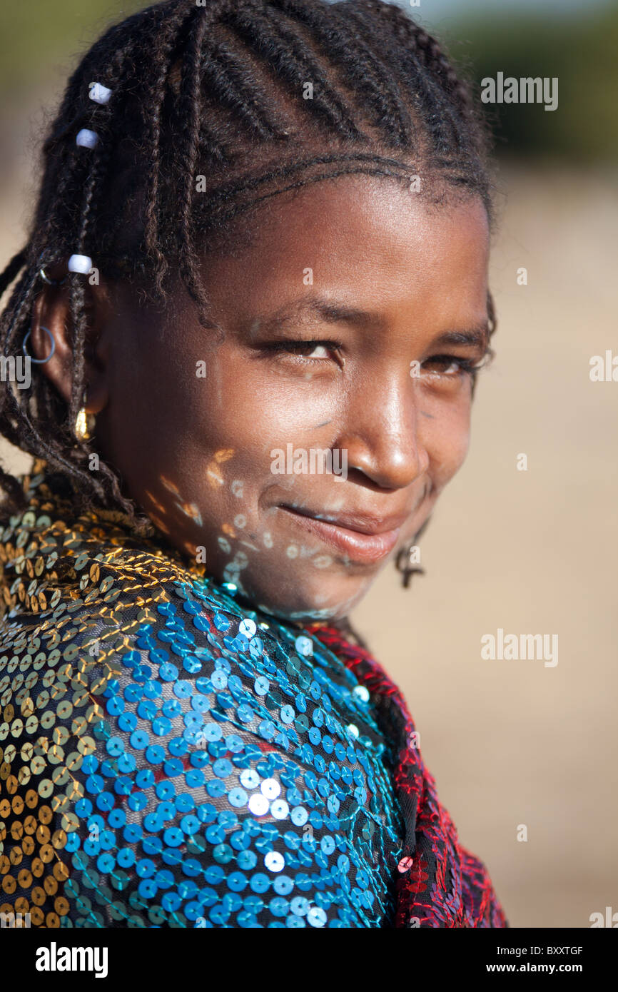 In a seasonal Fulani village in northern Burkina Faso, reflections from the sequins of a young woman's shawl dance on her face. Stock Photo