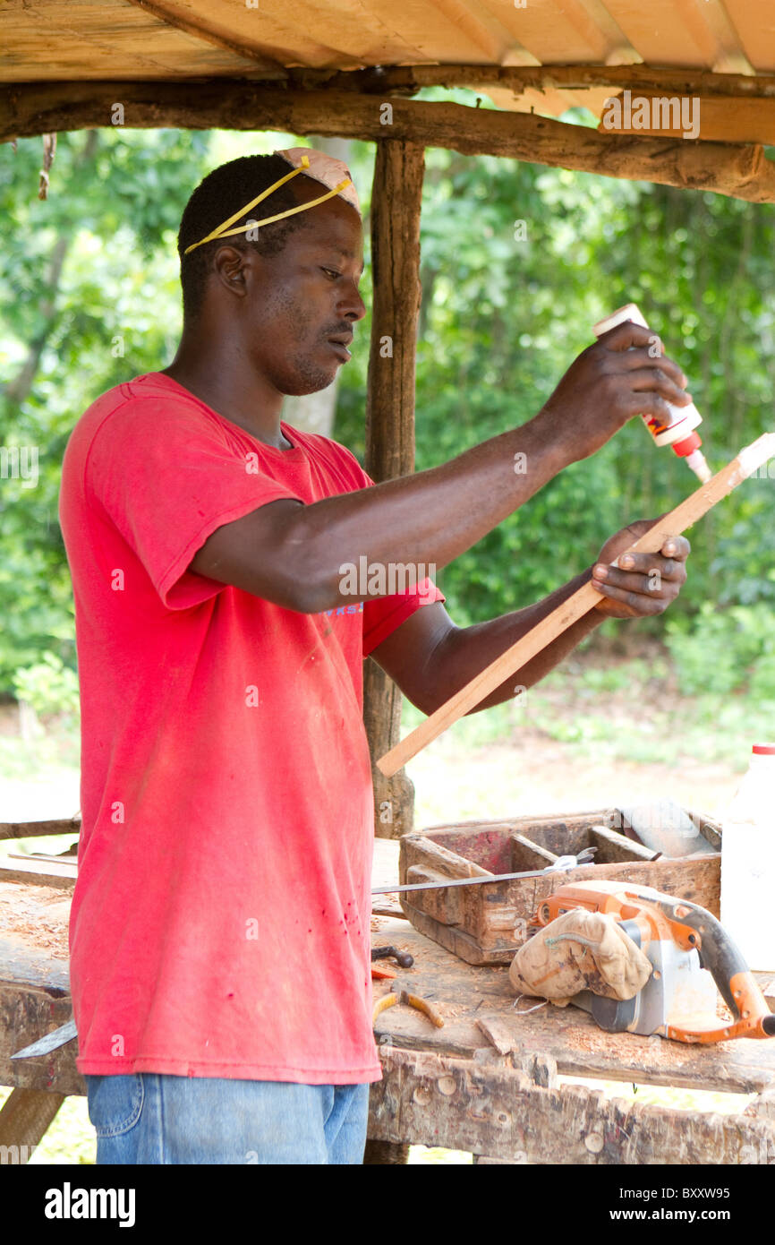 Jamaican carpenter applies glue to a piece of cedar wood for a cabinet ...