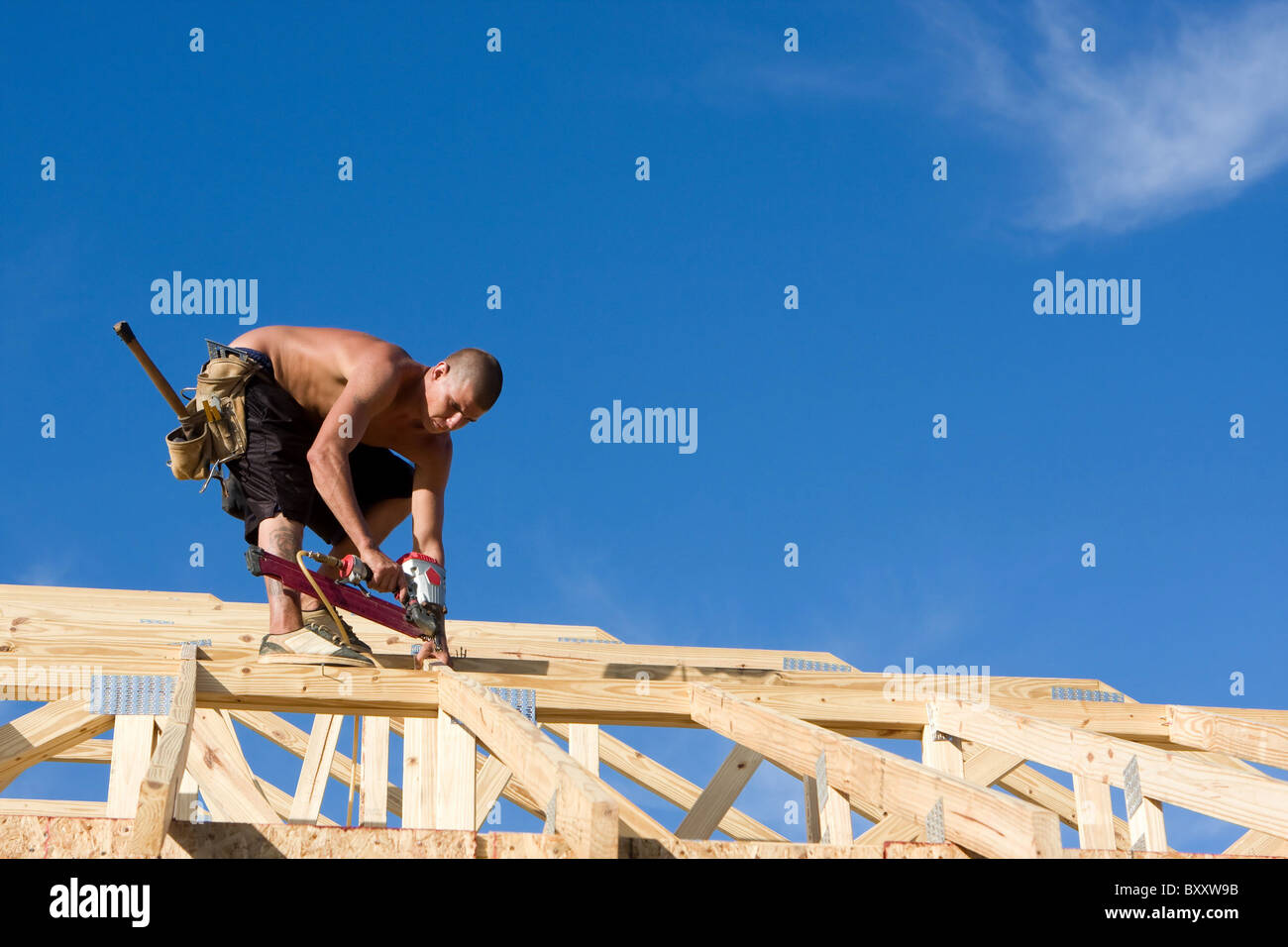 Carpenter uses a pneumatic nail gun to attach rafters and braces to a