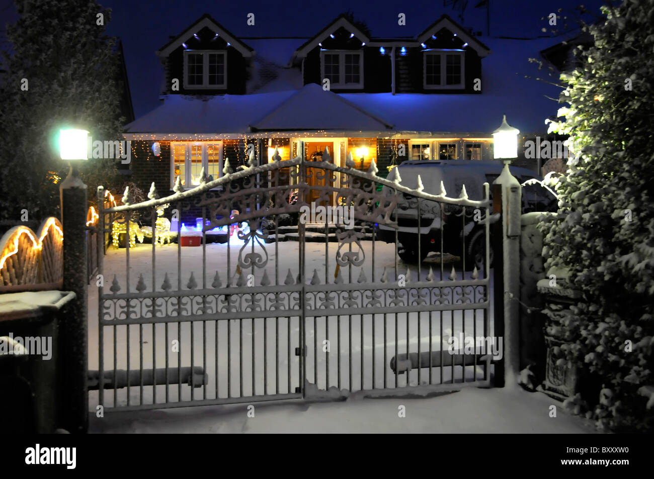 Winter weather snow covering front garden of electric gated house with lights & white Christmas decorations snowfall on roof Essex England UK Stock Photo