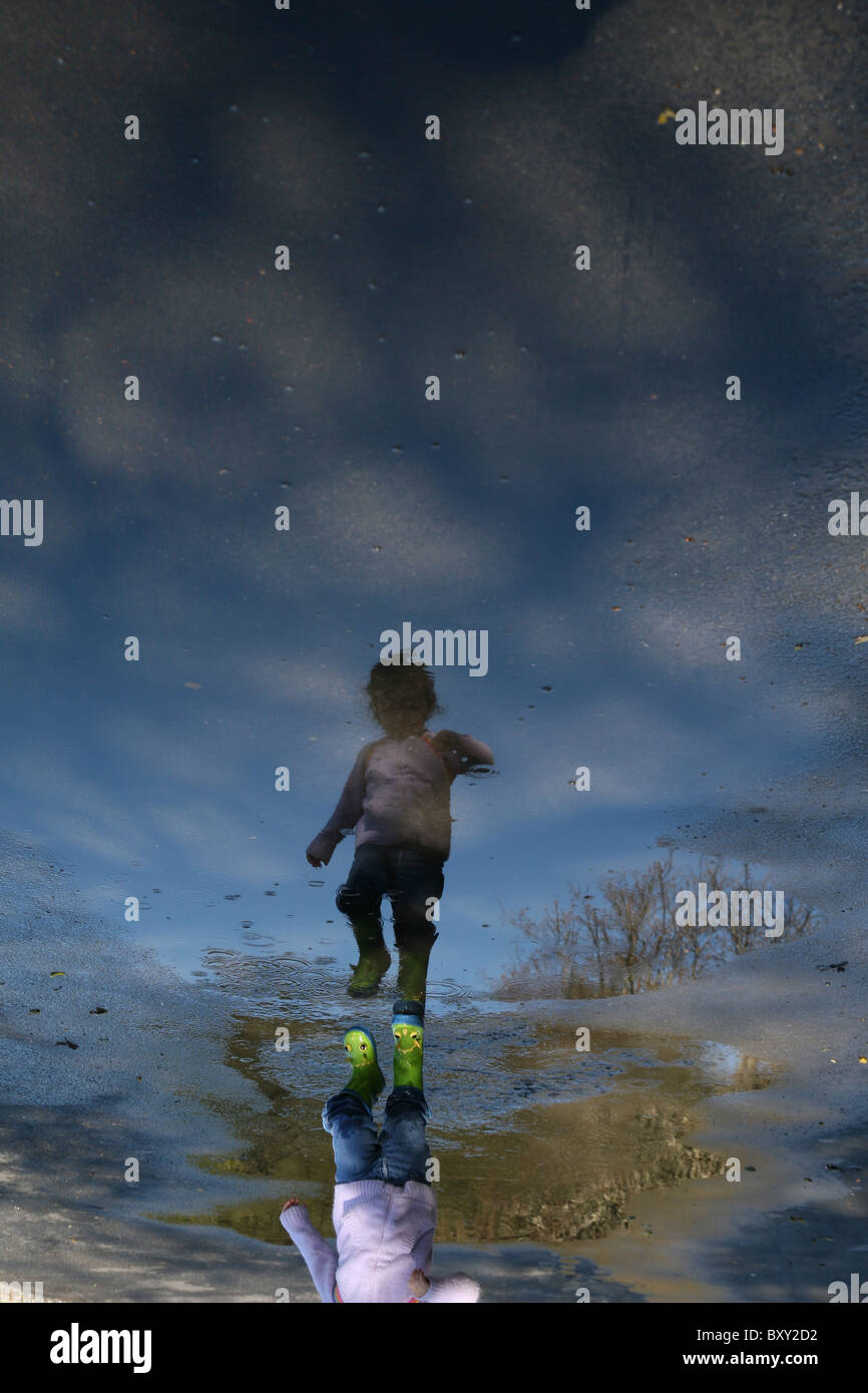 A young child walking through a puddle full of cloud reflections. Stock Photo