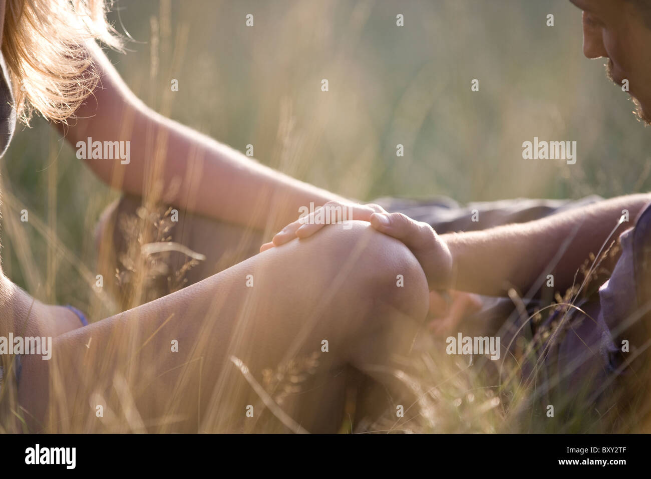 Detail of a young couple outdoors, mans hand on the womans knee Stock Photo