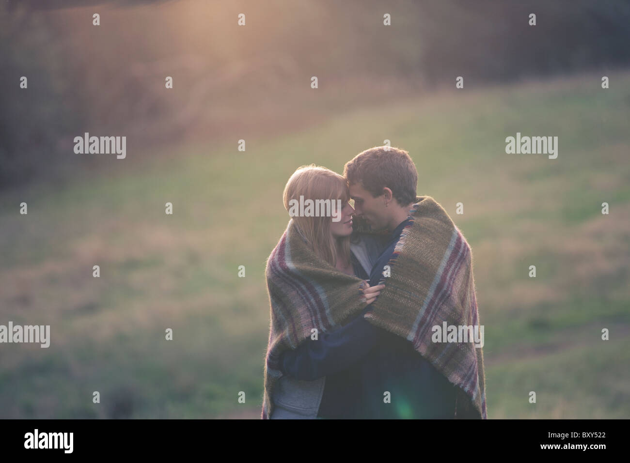 A young couple embracing outdoors, wrapped in a blanket Stock Photo