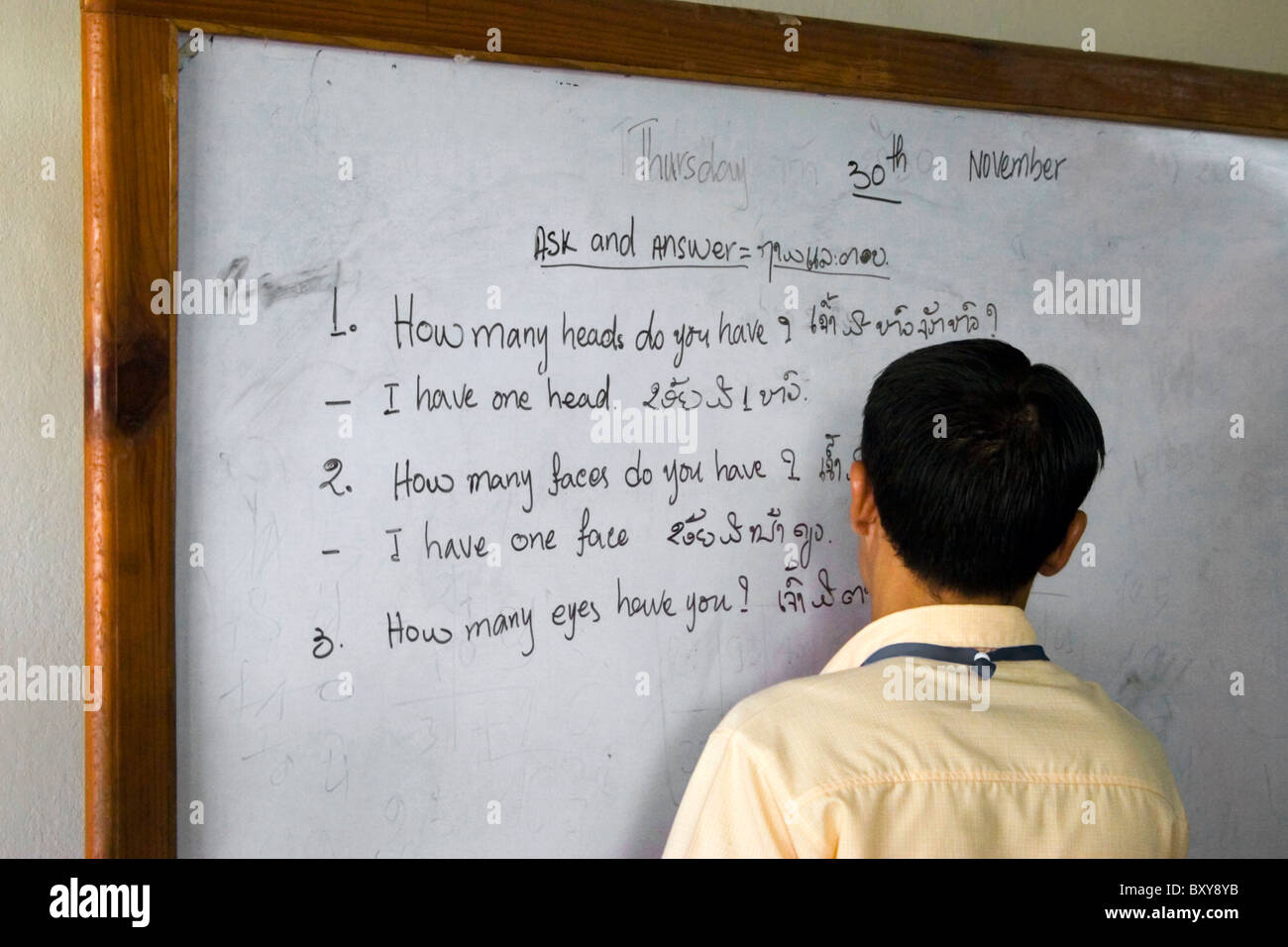 An Asian male English teacher is writing on a board with a black felt tipped marker in a hospital classroom in communist Laos. Stock Photo