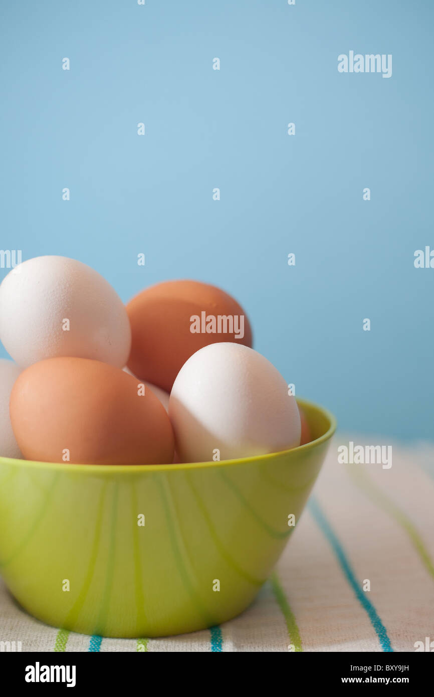 Brown and white chicken eggs in a green bowl on a striped tea towel with a blue background Stock Photo