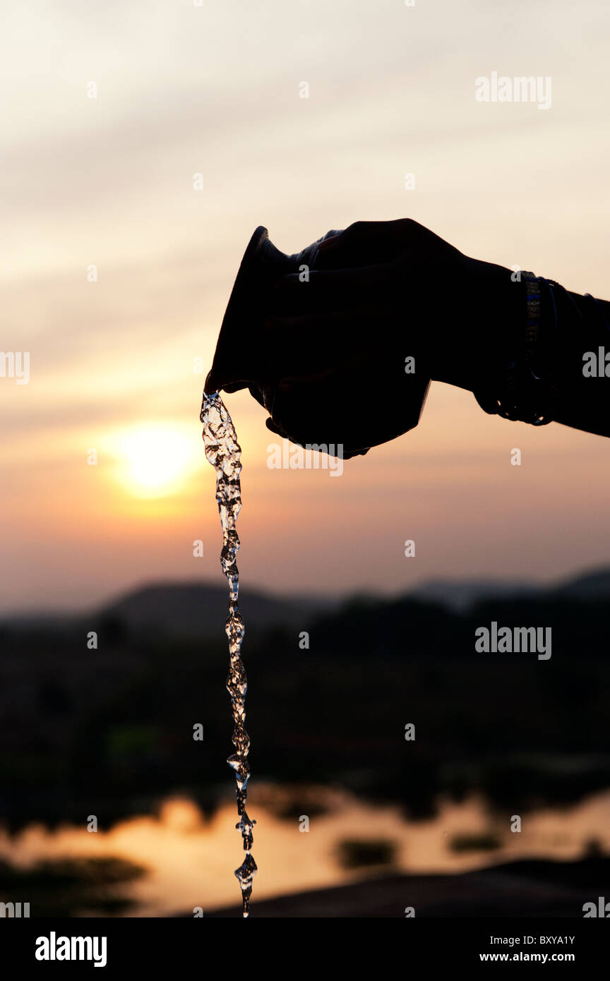 Indian childs hands pouring water from a pot at sunset. India Stock