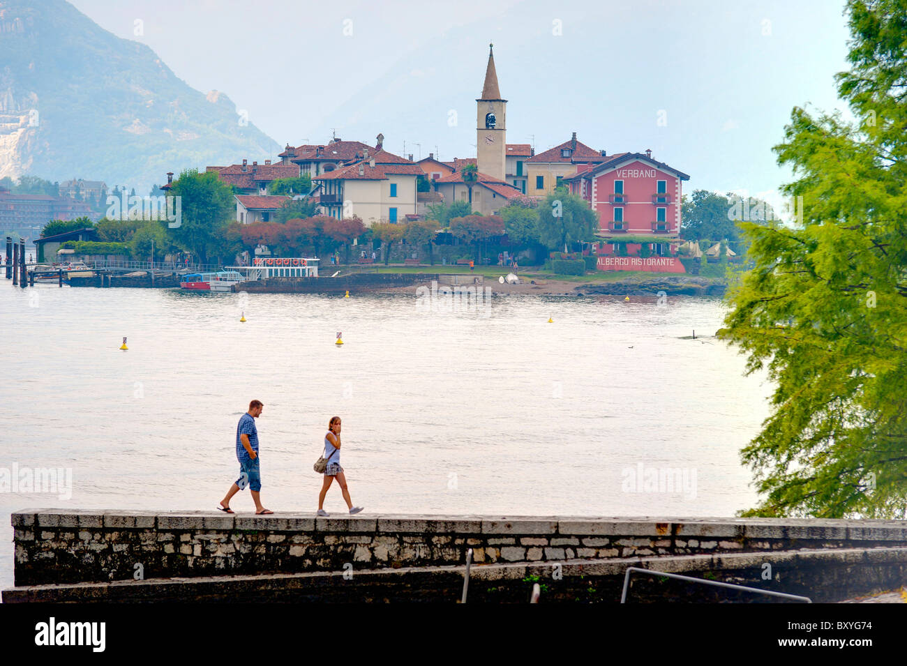 Couple walking on Isola bella with Isola dei Pescatori in the far distance Lago Maggiore Italy Stock Photo