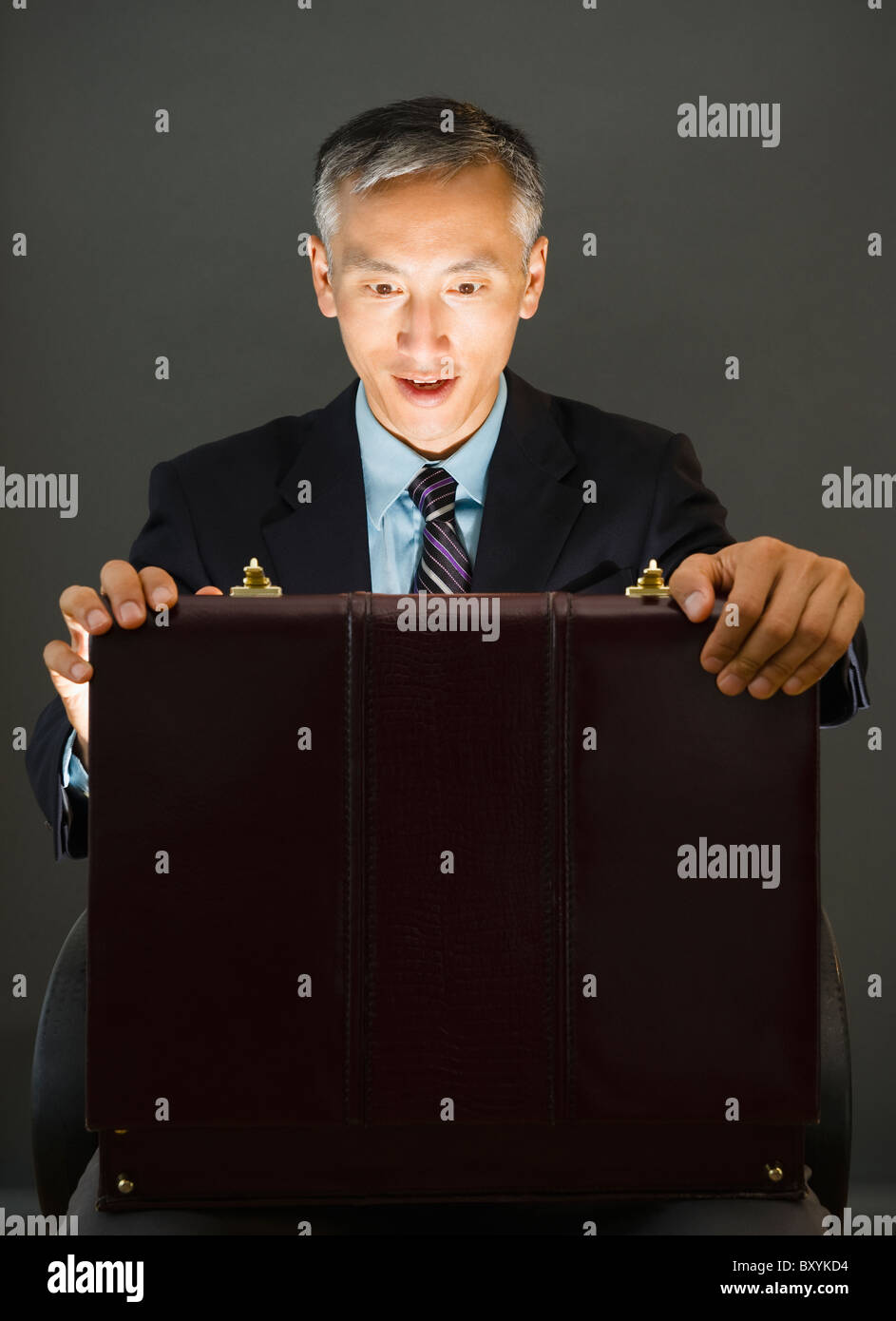 Surprise businessman looking into open briefcase, studio shot Stock