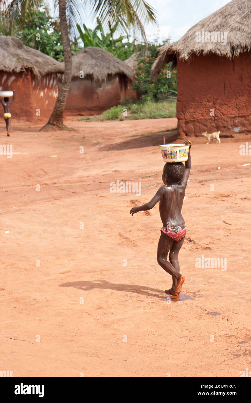 A young African child living in rural Togo balances water on her head while transporting it from