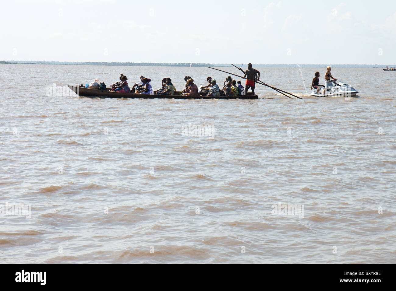 A traditional West African canoe transports villagers from Togoville across Lac Togo while a modern jet ski zips by. Stock Photo