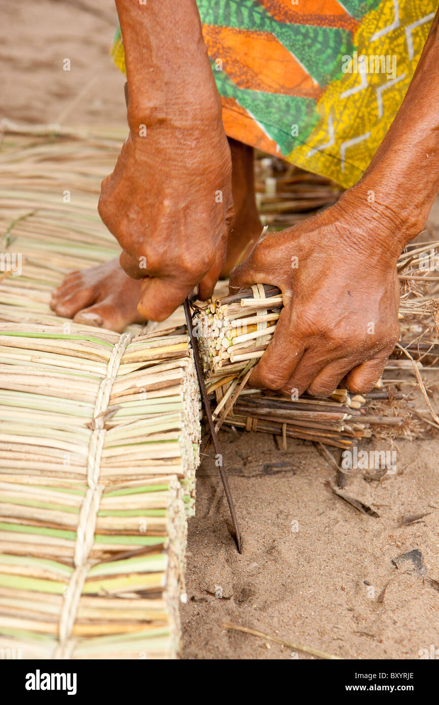 A woman trims extra reeds from a hand made mattress in west Africa as part of an income generation project run by an NGO. Stock Photo