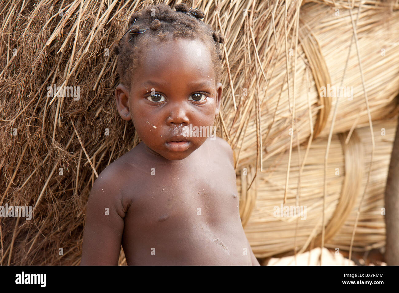 An African kid stands with piles of reeds in the background. His village participated in an income generation project by an NGO. Stock Photo
