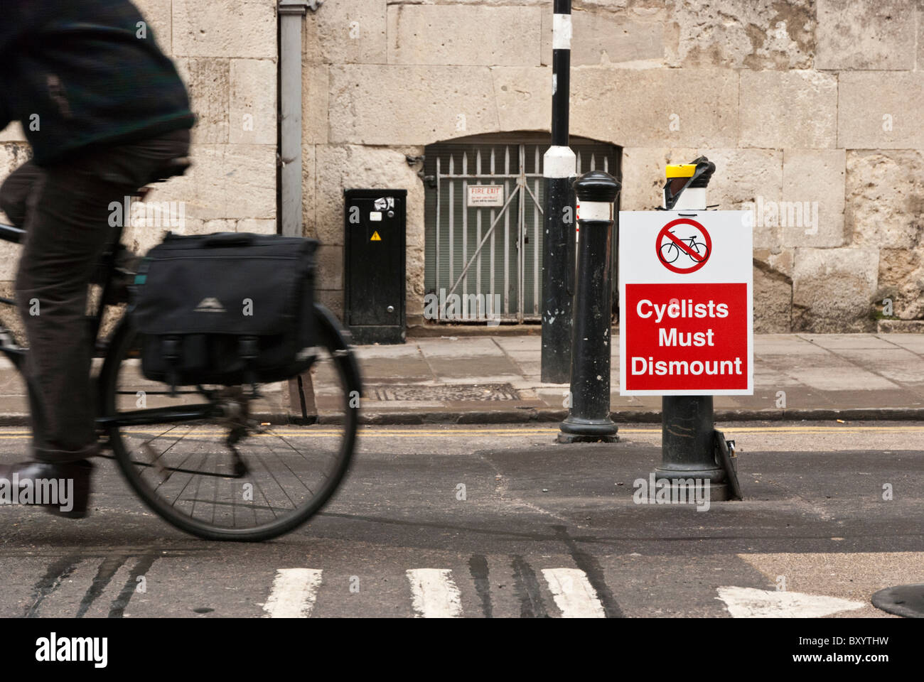 Cyclist riding past a sign ordering cyclists to dismount in Broad Street, Oxford, Oxfordshire, UK. Stock Photo