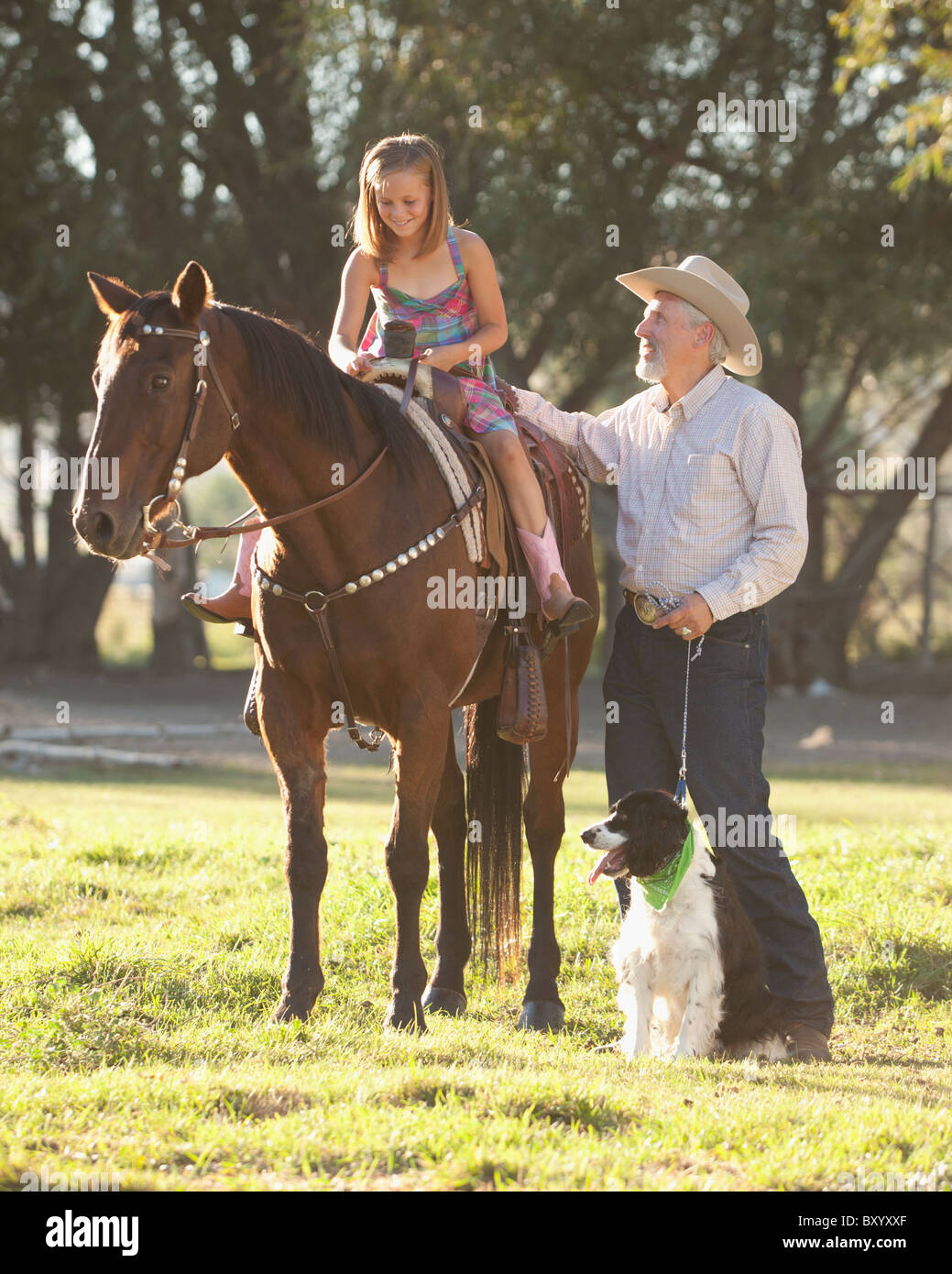 Senior man with dog assisting granddaughter horseback riding in ranch Stock Photo