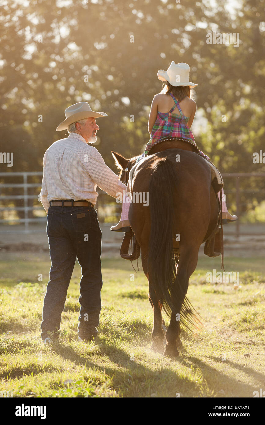 Senior man assisting granddaughter horseback riding in ranch Stock Photo