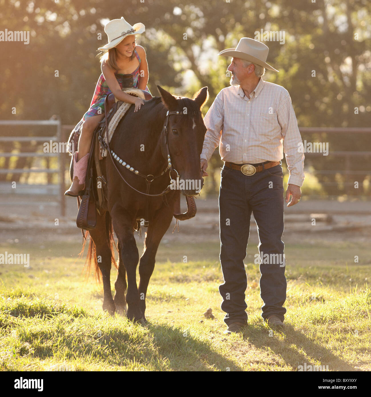 Senior man assisting granddaughter horseback riding in ranch Stock Photo