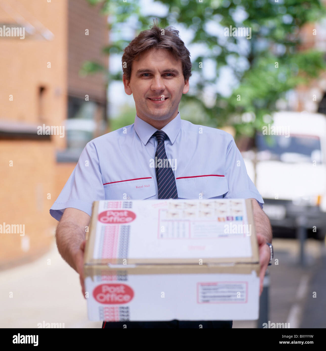 Royal Mail postman with a package in England in Great Britain in the United Kingdom.Occupation Work Postal Delivery Service Stock Photo