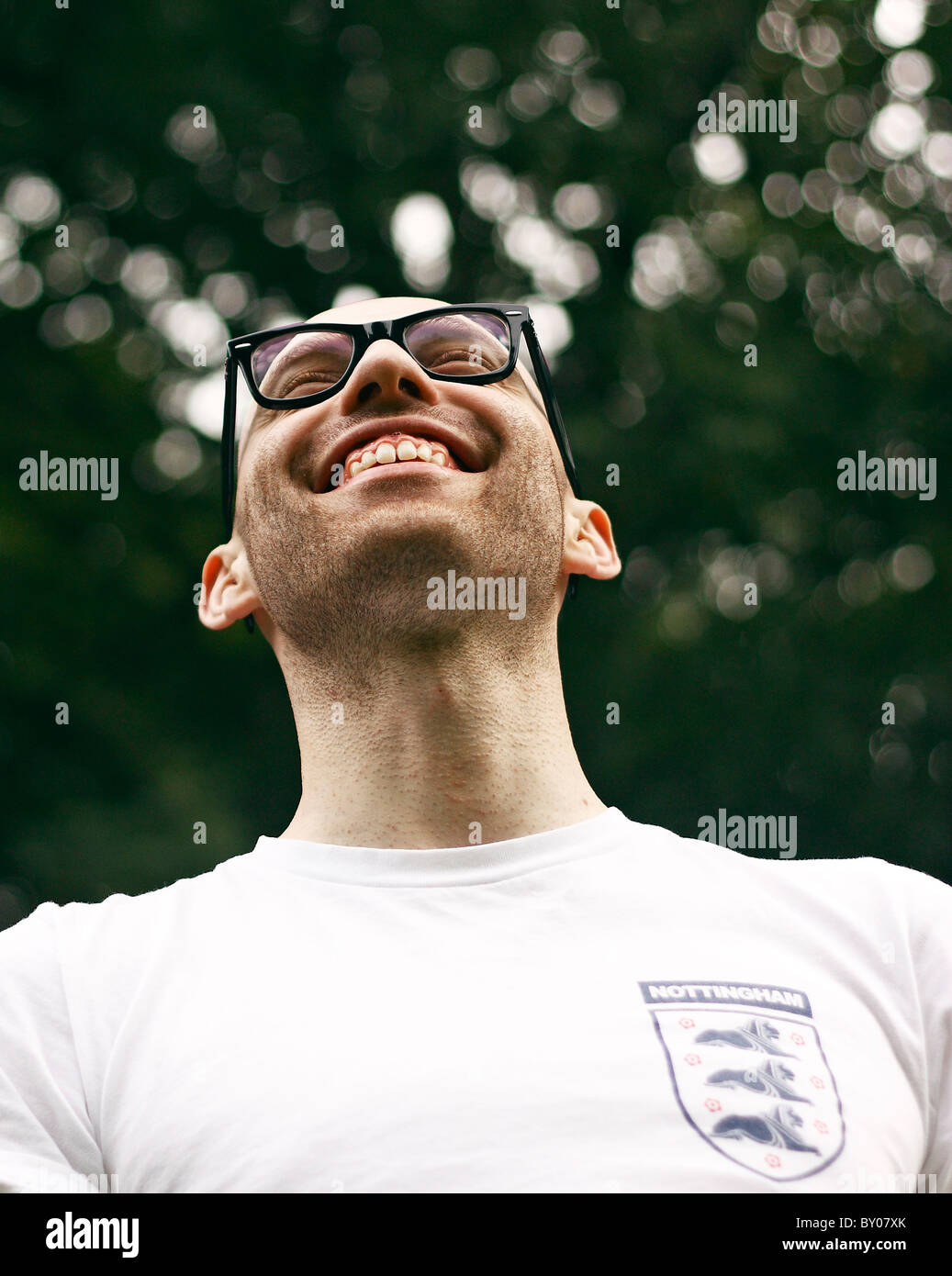 A young man smiling, wearing glasses and a retro England football shirt