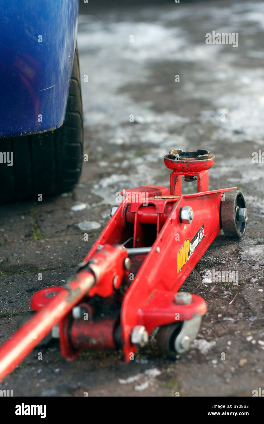 A close up of a red hydraulic trolley jack next to a car on an icy driveway. Stock Photo