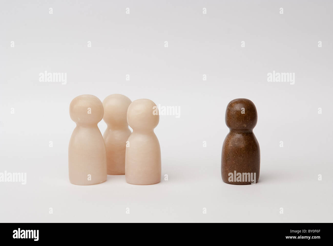 A group of 3 white figures and 1 brown figure, standing seperate Stock Photo