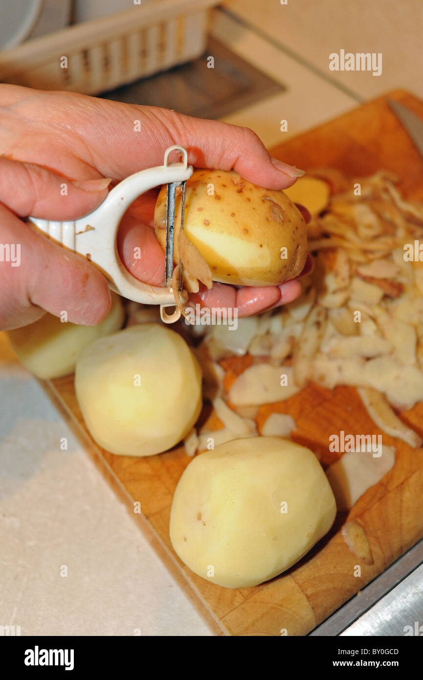 Peeling potatoes with peeler in a kitchen Stock Photo