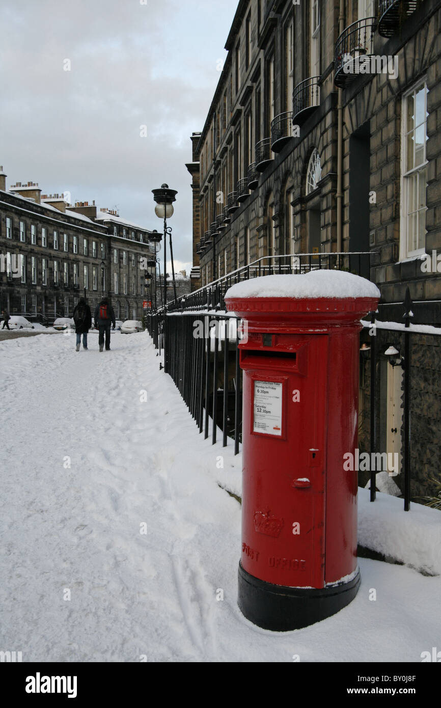 A red Royal Mail post box, covered in snow, in a street in central