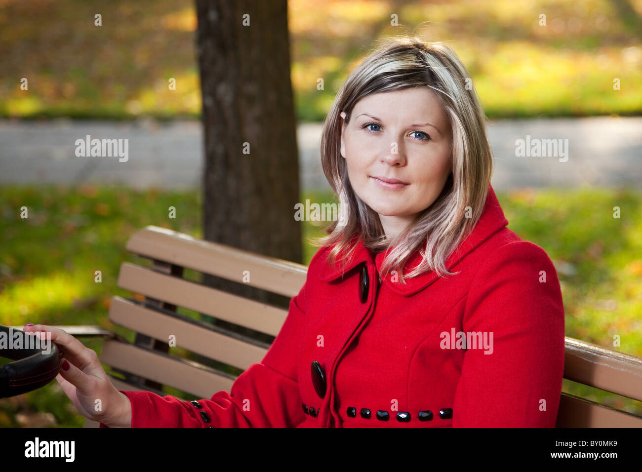 Blond woman in red coat holding handle or pram. Stock Photo