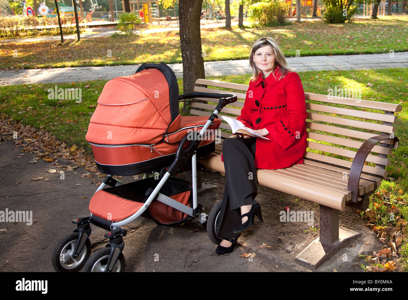 Young woman reading book on bench with a pram. Stock Photo