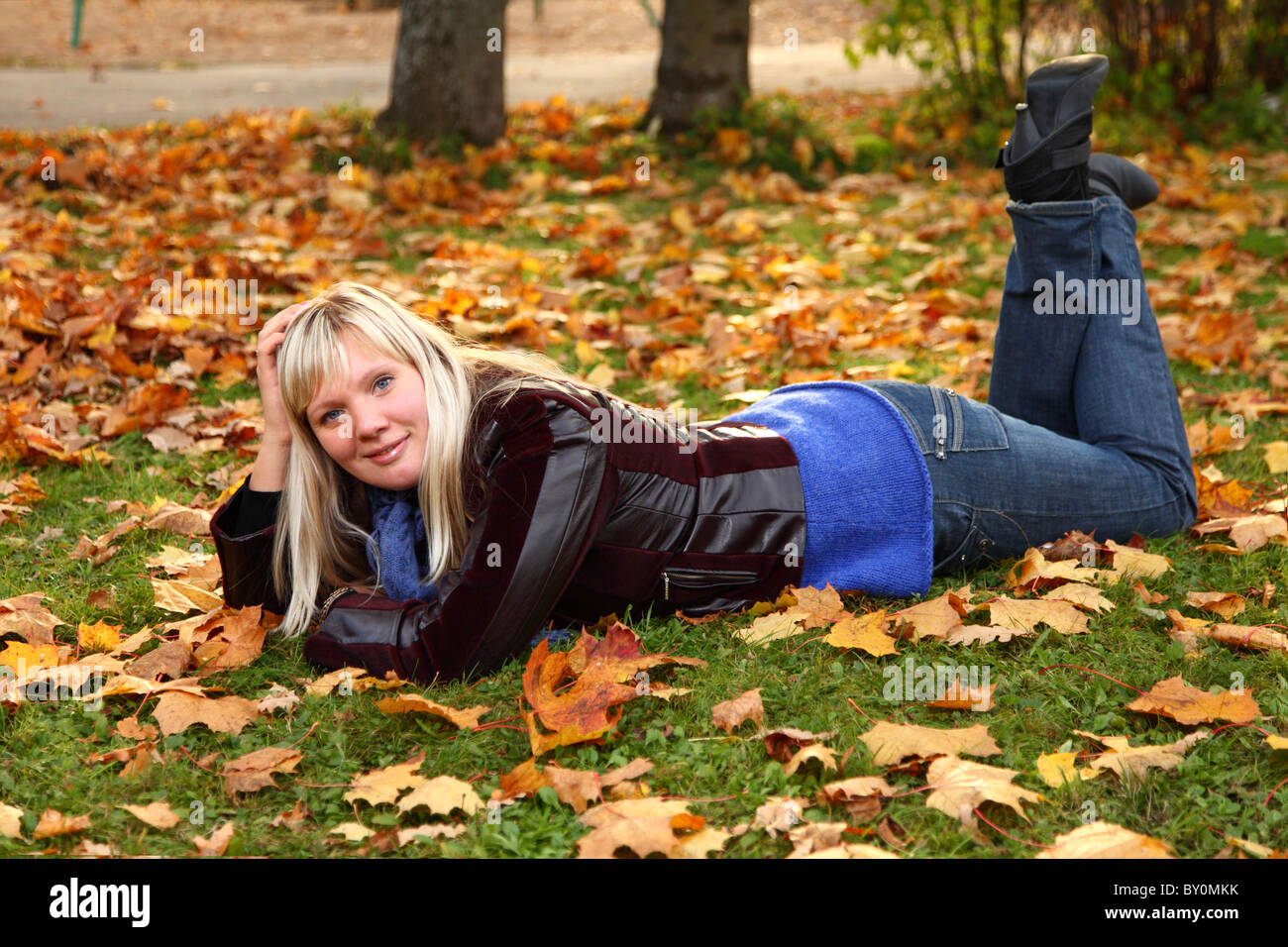 Caucasian blond girl in black leather jacket lying on grass. Stock Photo