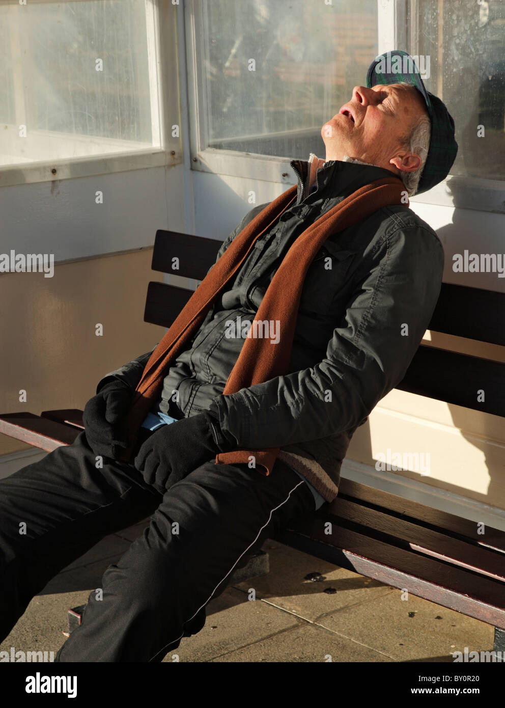 Old man asleep in a seaside shelter. Stock Photo