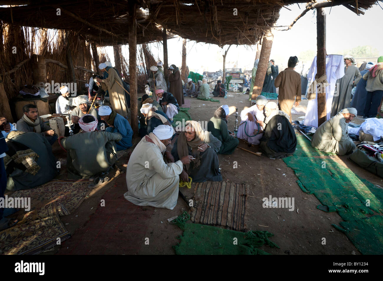 Men relaxing, talking, smoking and tea drinking in a shelter at Luxor Camel Market Egypt Africa Stock Photo