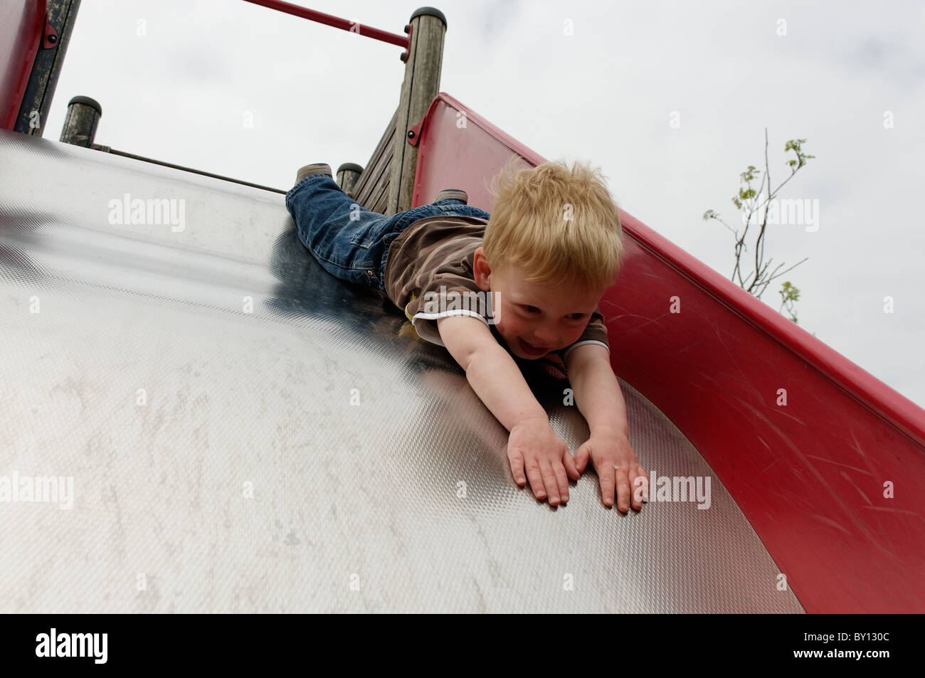 A young boy sliding head first on a park slide Stock Photo
