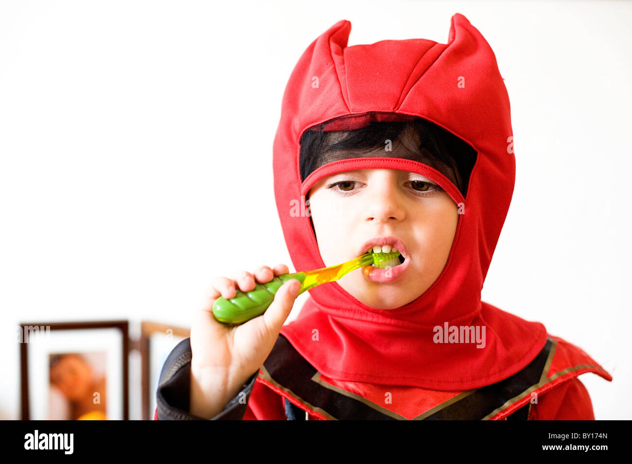 Five year old boy dressed up in a superhero costume brushing his teeth