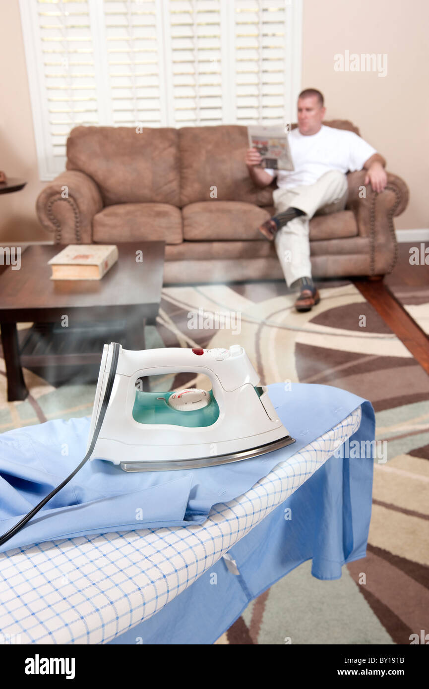 A man sit on his couch while the iron burns and scorches his dress shirt. Stock Photo