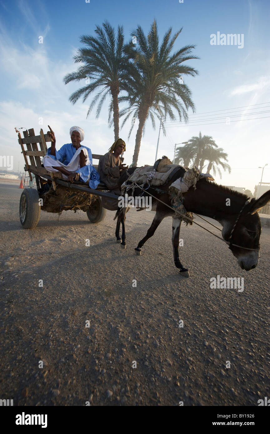 Two Egyptian men sit in cart pulled by donkey along dusty desert track Stock Photo