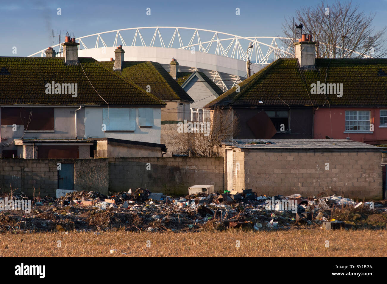 Dilapidated housing with piles of rubbish dumped in Limerick city, Ireland, with the Munster sports stadium in the background. Stock Photo