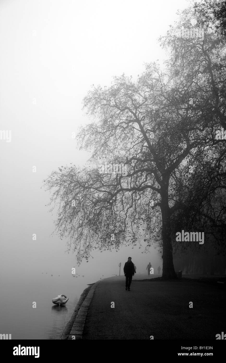 Pedestrians walking along the side of a misty Serpentine Lake, Hyde Park, London, UK Stock Photo