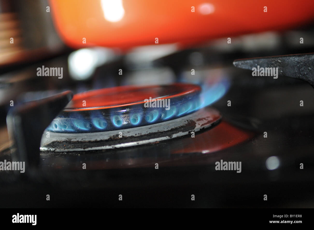 Closeup of blue gas flames burning on a cooker hob with an orange pan