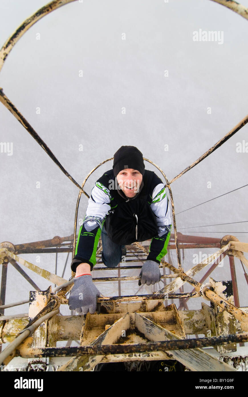 A man climbing up a metal ladder on the outside of a radio antenna