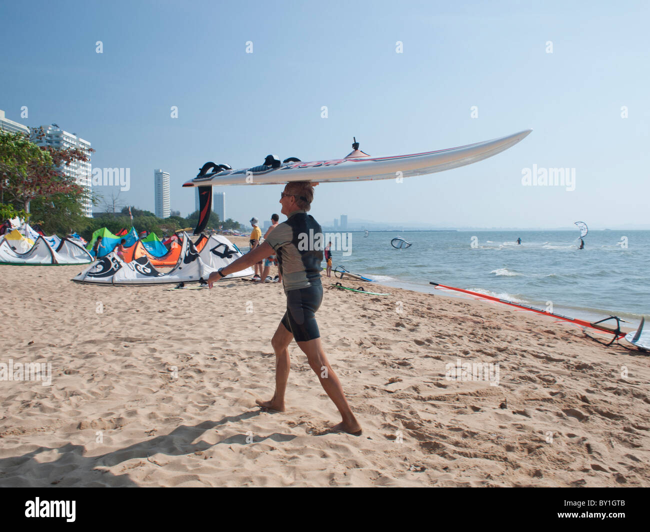 An old man carrying his windsurfing board after finished sailing. Stock Photo